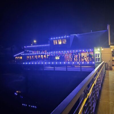 Tides Tavern lit up with blue Trimlight commercial lighting at night, with reflections on water.