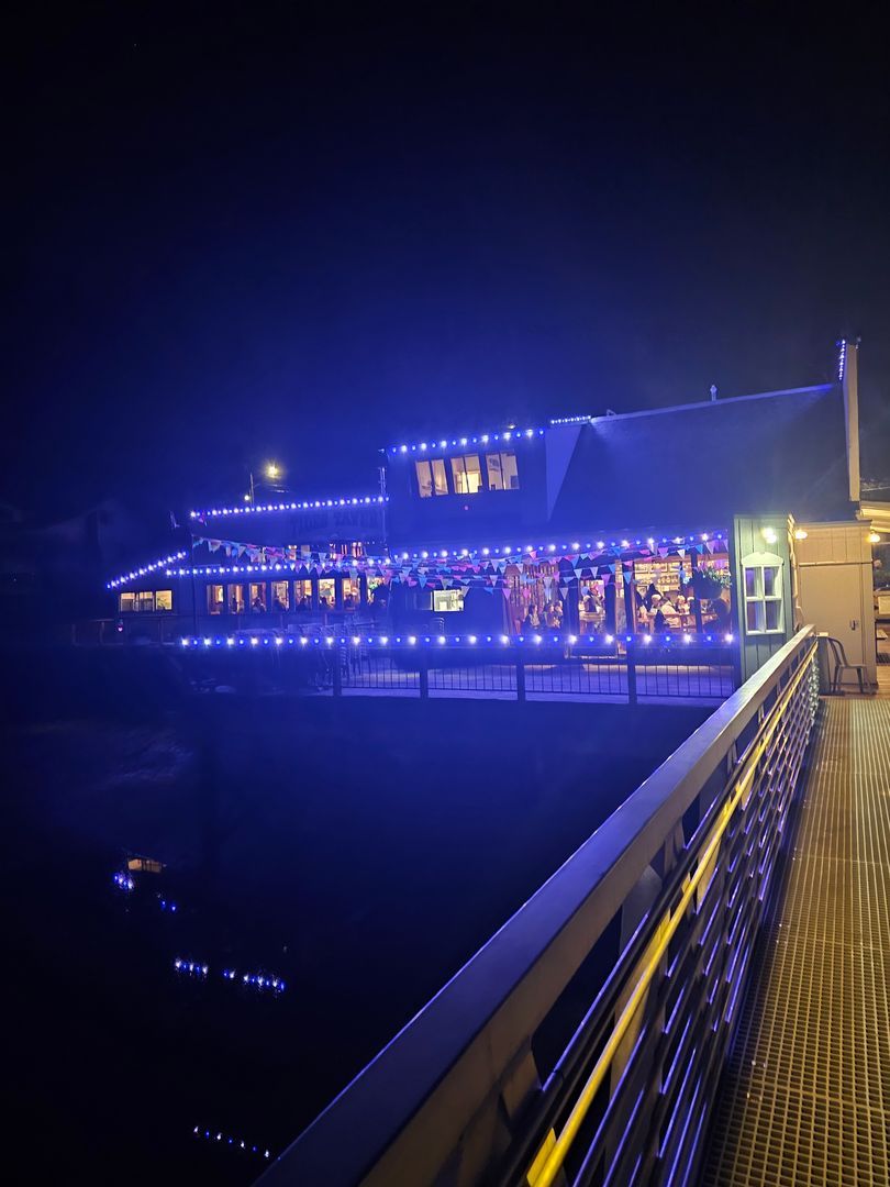 Tides Tavern lit up with blue Trimlight commercial lighting at night, with reflections on water.