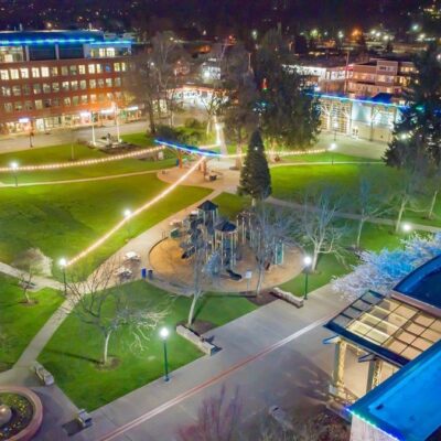 Aerial nighttime view of a downtown park in Puyallup with multicolored lights and active pedestrians.