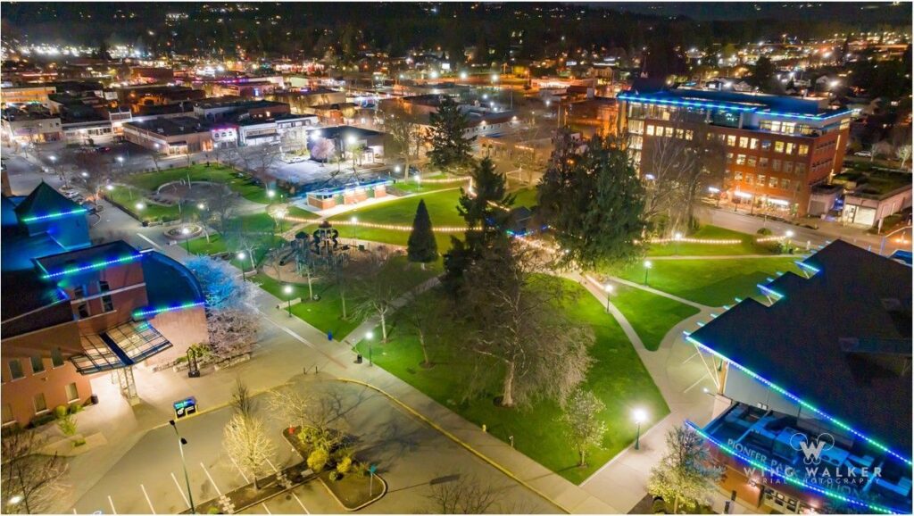 Aerial nighttime view of downtown Puyallup with colorful building lights and a lit park.