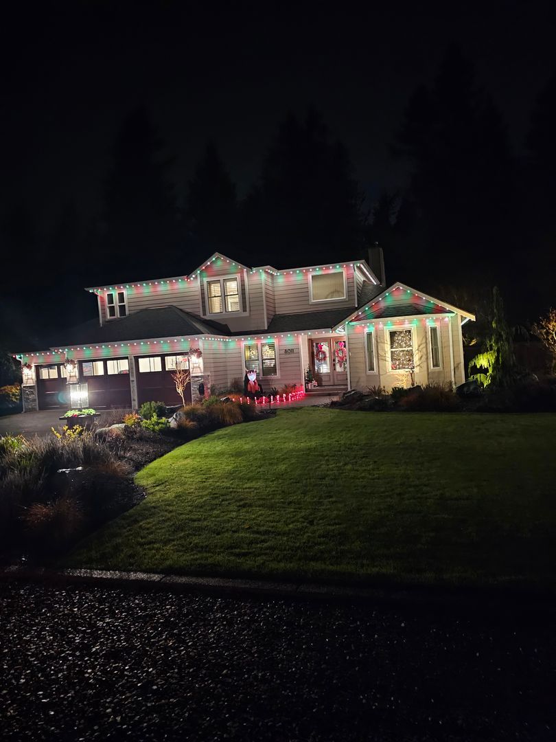 Exterior view of a two-story house at night with permanent colorful lights installed along the roof and festive decorations on windows.