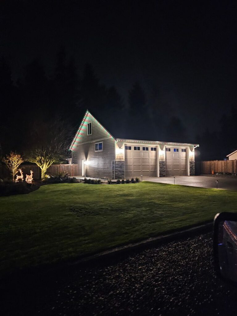 A nighttime image of a two-story house with red and green lights installed along the roofline and over the garage doors.