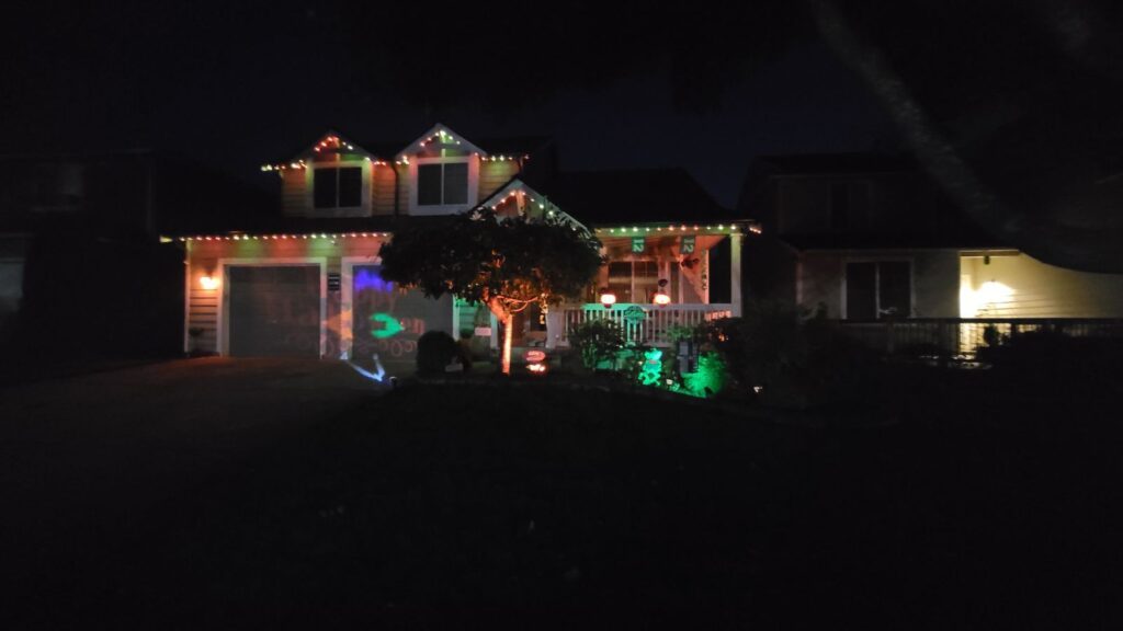 A two-story house decorated with colorful lights and illuminated decorations in a residential neighborhood at night.